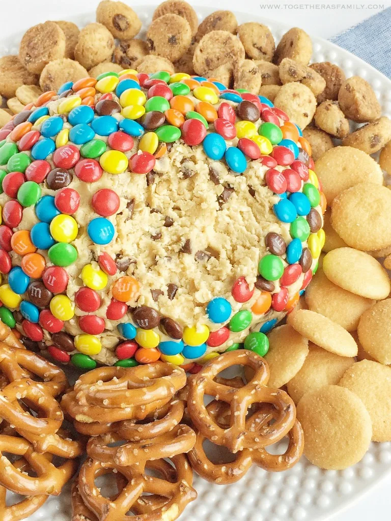 giant cookie dough cheeseball coated in m&ms, surrounded by mini cookies, pretzels, and wafers