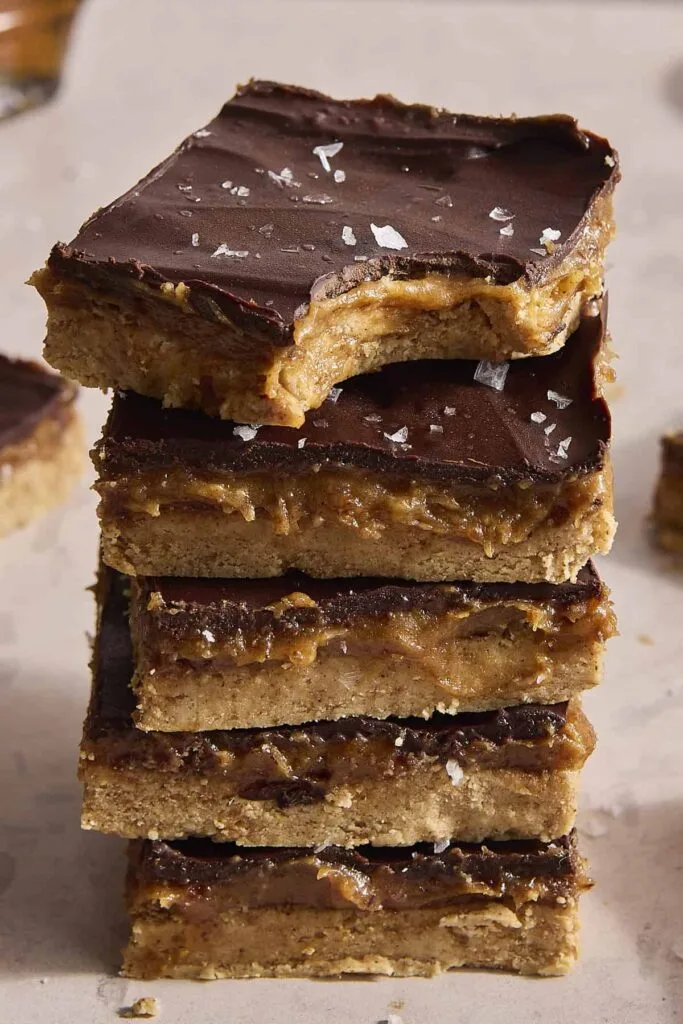 stack of chewy bars with chocolate topping, caramel layer, and flaky salt on top