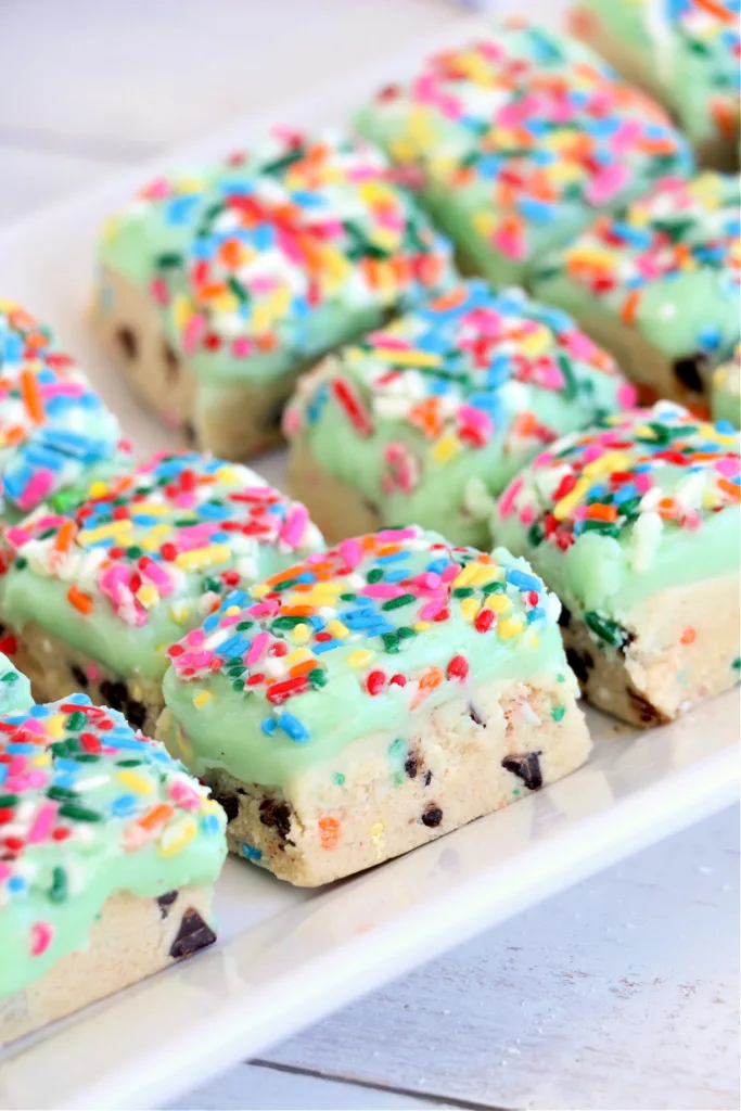 soft, frosted squares topped with green icing and rainbow sprinkles stacked on a white table